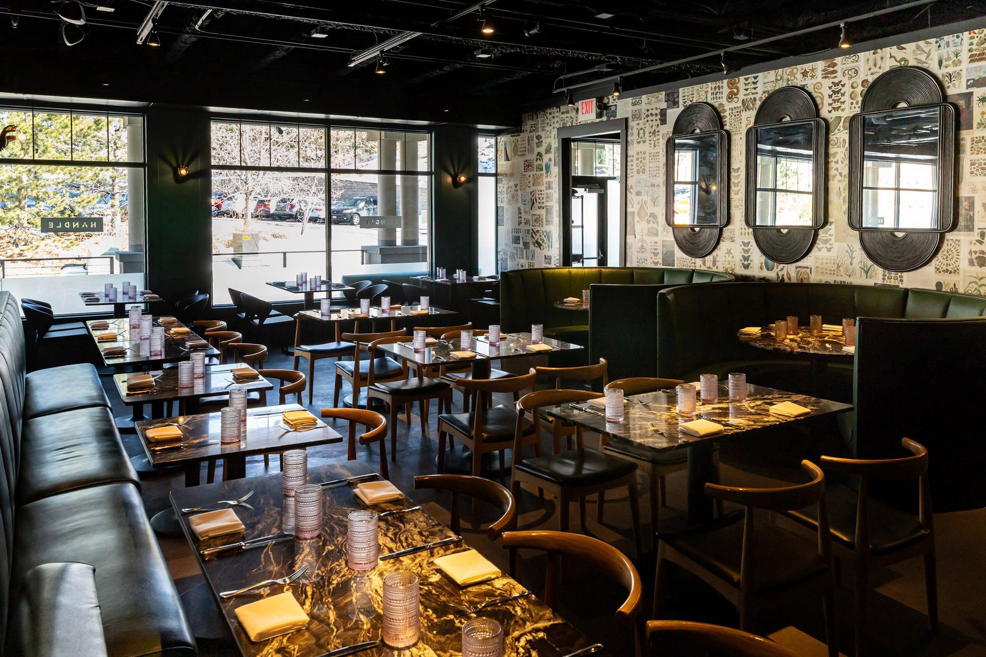 Interior of a restaurant with tables, chairs, booths, large windows, and patterned wallpaper.