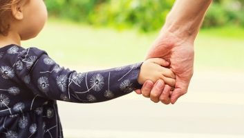 A little girl is holding a man 's hand.