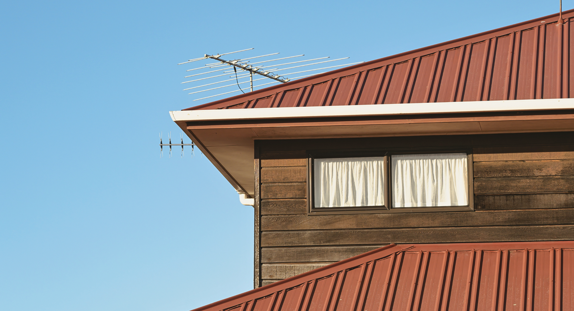 A wooden building with a red roof and two windows