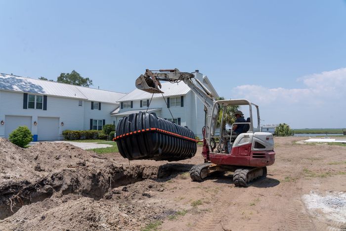a white and red excavator is lifting a large black tank