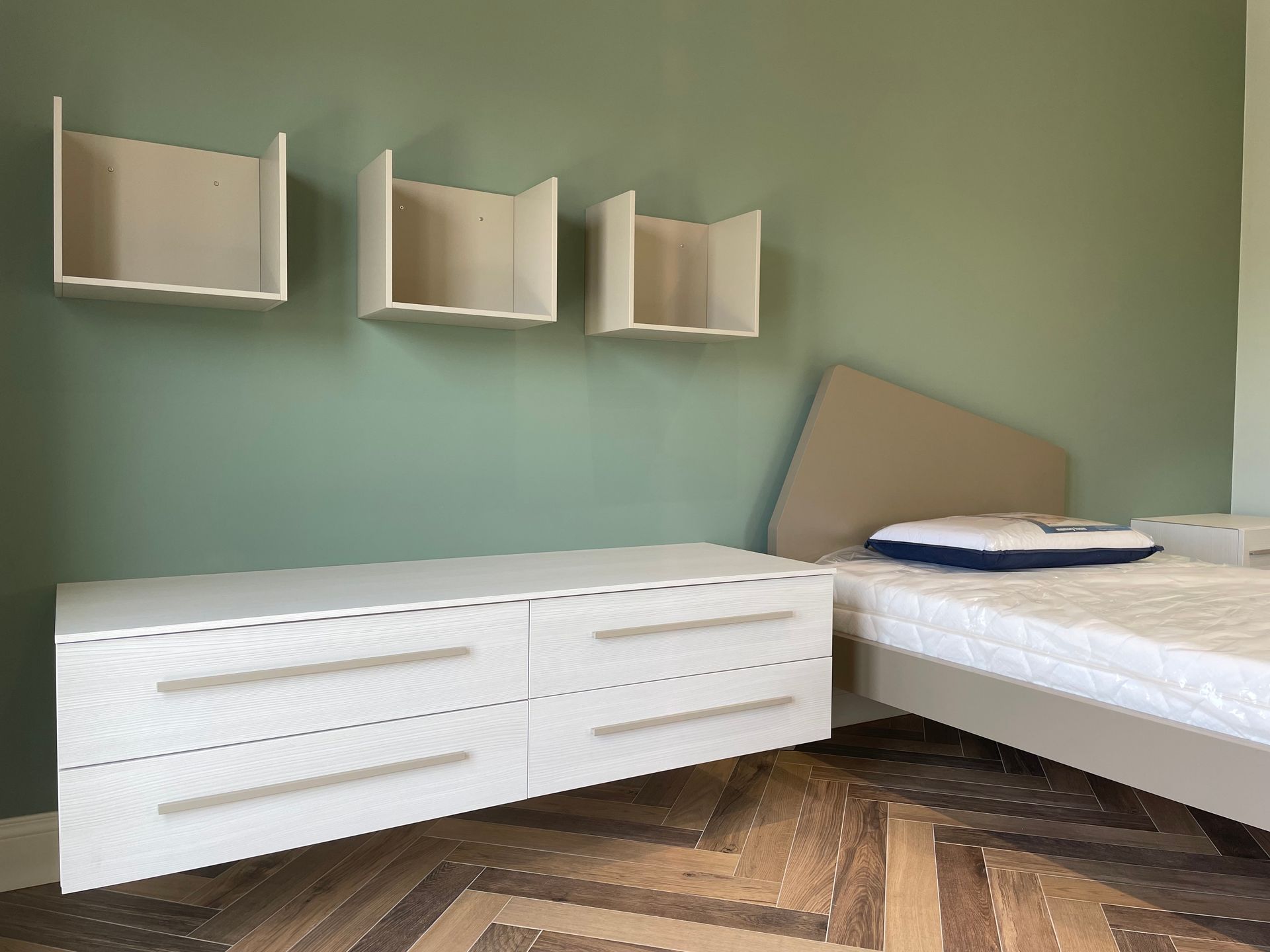 camera da letto con letto, cassettiera e mensole a muro.