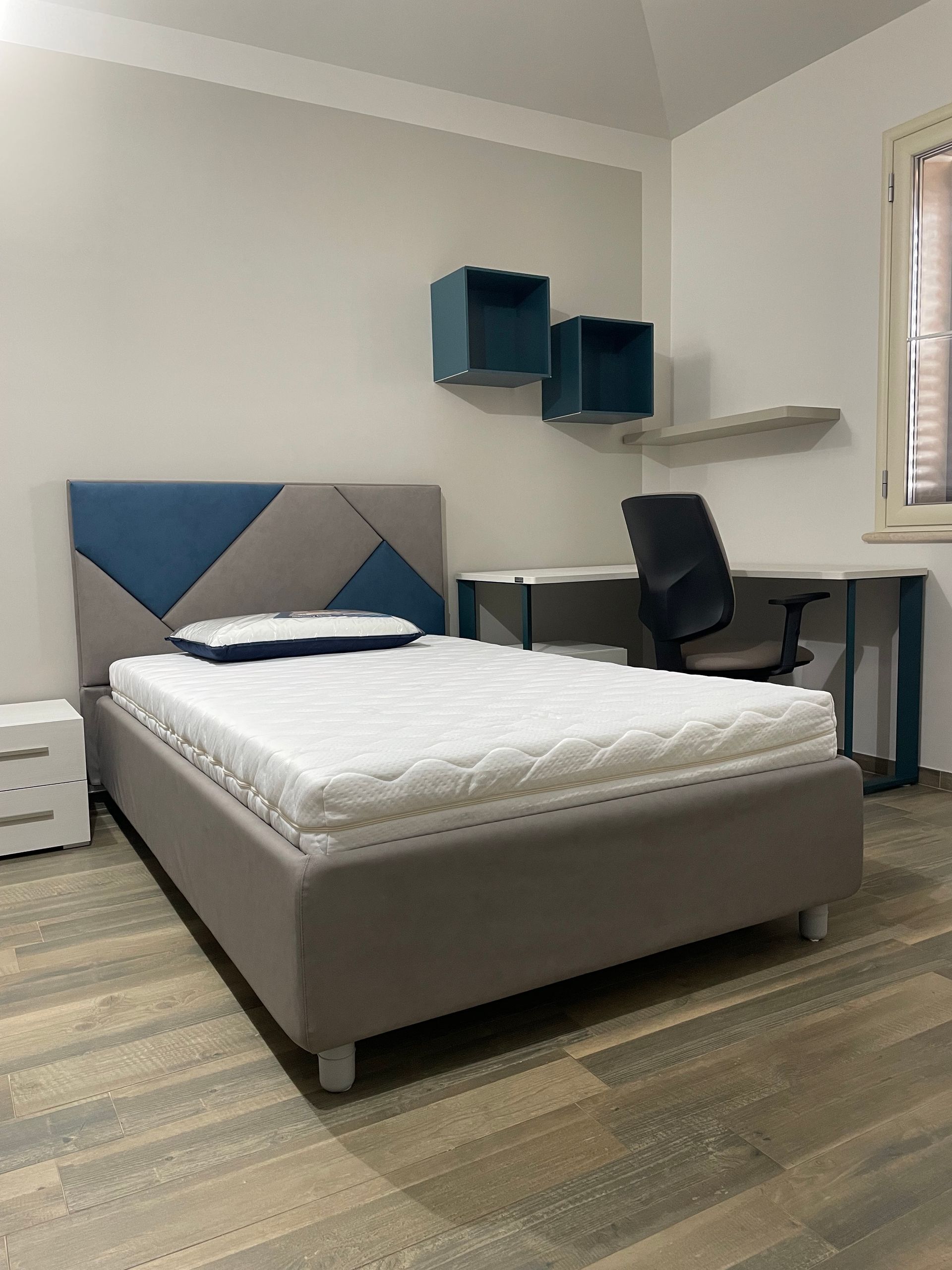 Una camera da letto con letto, scrivania, comodino e sedia.