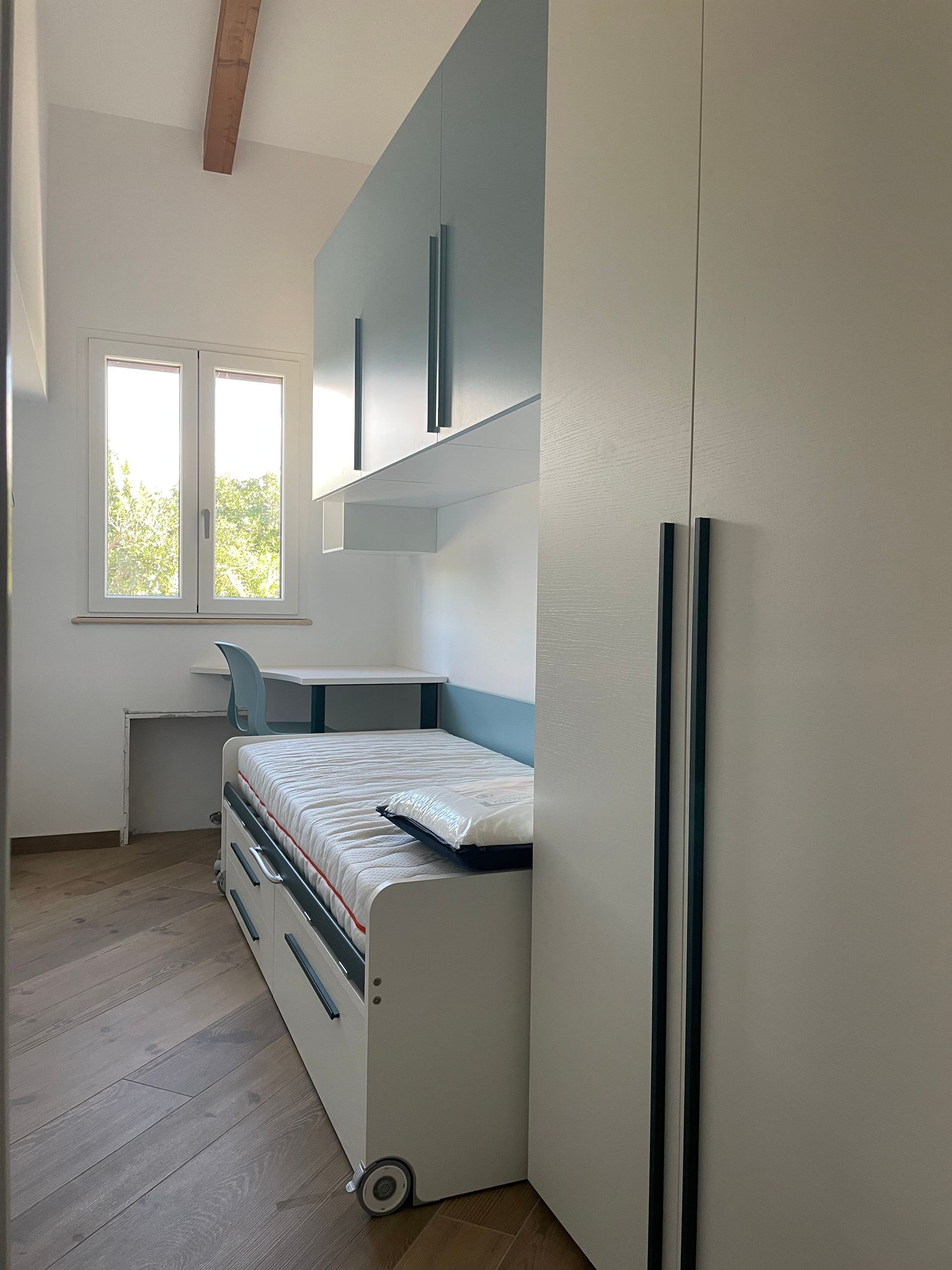 Una camera da letto con letto, scrivania, armadietti e finestra.