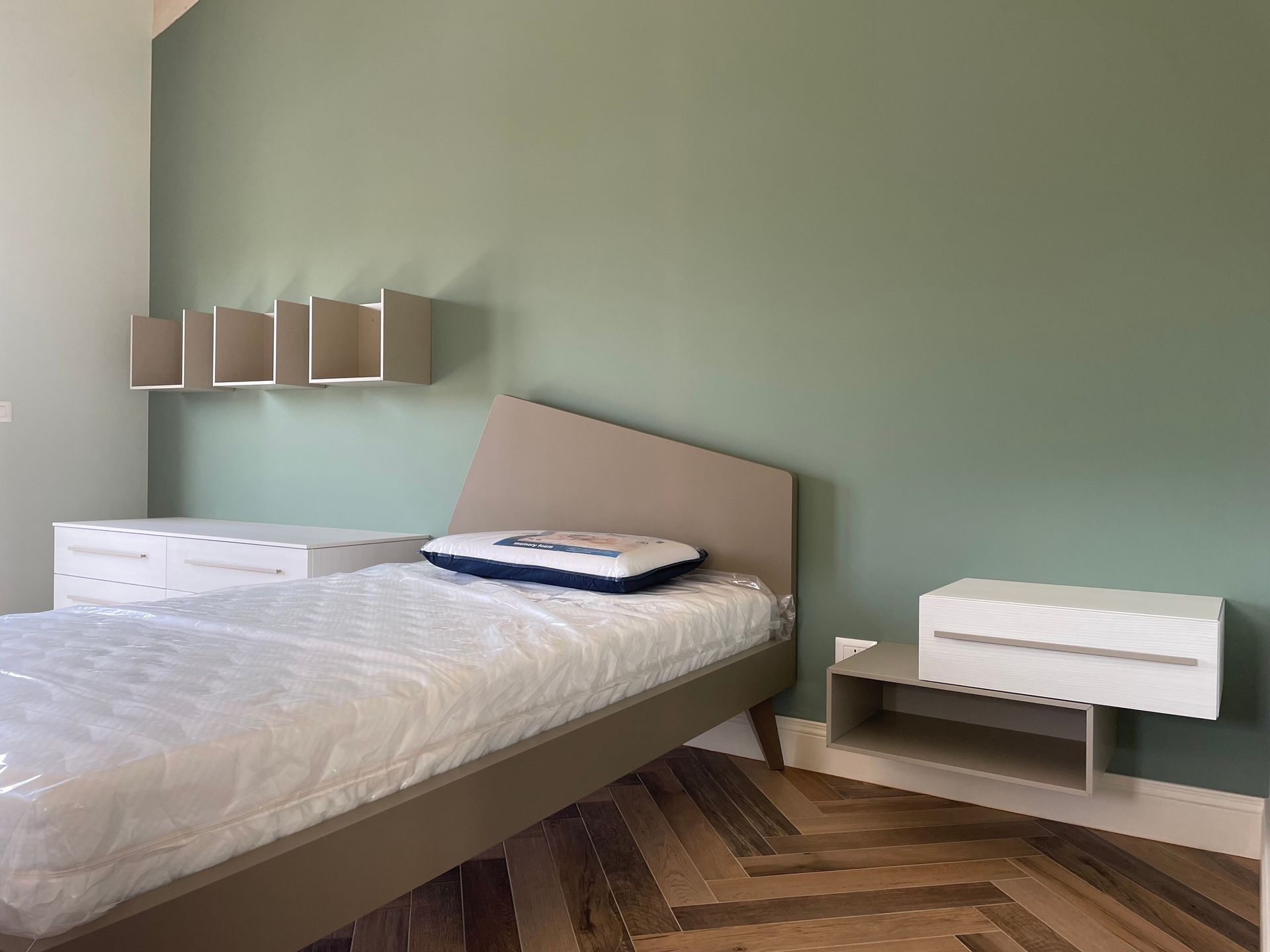Una camera da letto con letto, comodino, cassettiera e pareti verdi.