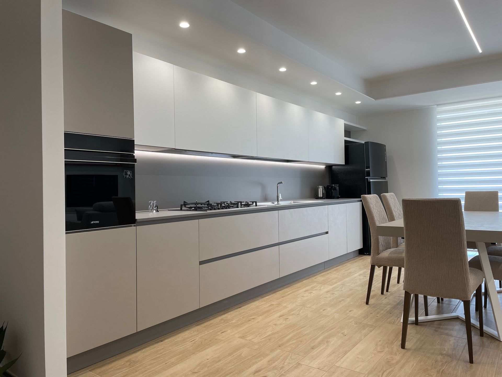 Una cucina con mobili bianchi e pavimenti in legno, tavolo da pranzo e sedie.