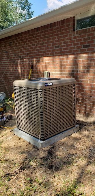 Outdoor air conditioner unit beside a brick house wall in a shaded yard