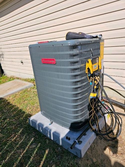Gray outdoor HVAC unit with yellow service equipment and coiled hoses beside a house wall