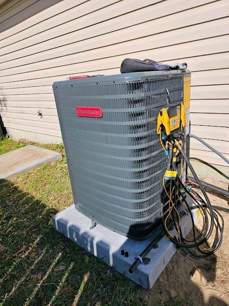Gray outdoor HVAC unit with yellow service equipment and coiled hoses beside a house wall