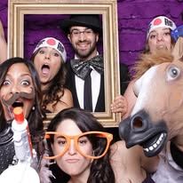 People in playful photo booth props posing in a frame, with a horse head and orange glasses in front