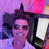 Smiling person in sunglasses posing in a pink-lit room with black display booths.