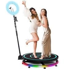 Two women on a rotating platform with a ring light and phone holder.