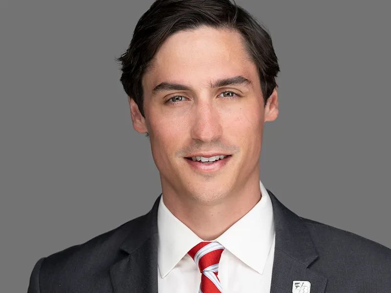 Portrait of a man in a dark suit and red striped tie against a gray background