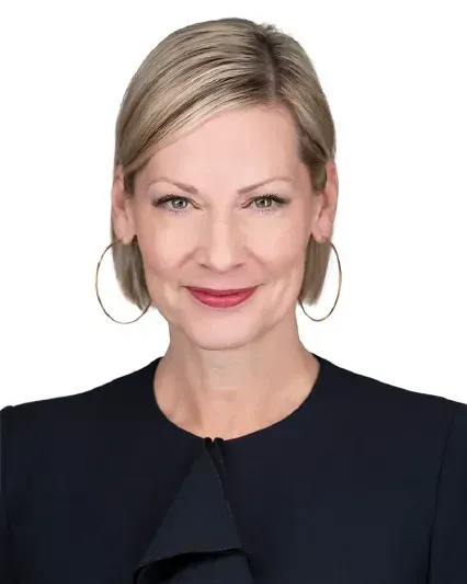Portrait of a smiling woman with blonde hair, hoop earrings, and a dark jacket on a white background