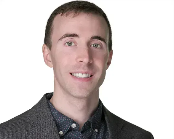Portrait of a smiling man in a gray blazer and dark shirt on a white background