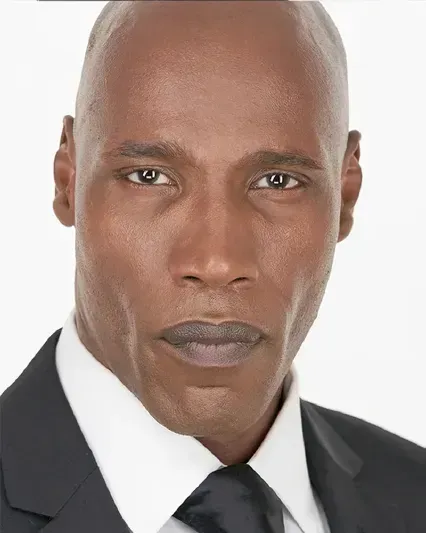 Studio headshot of a person in a black suit and tie against a white background