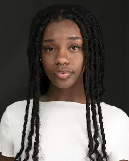 Portrait of a person with long braided hair wearing a white top against a dark background