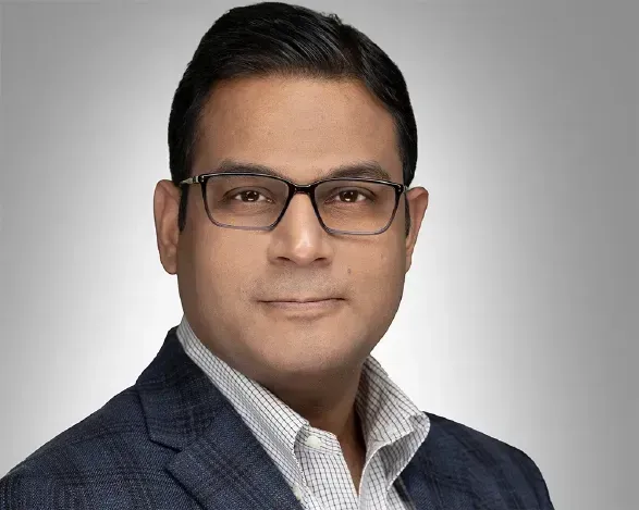 Headshot of a man wearing glasses, a navy blazer, and a white shirt on a gray background