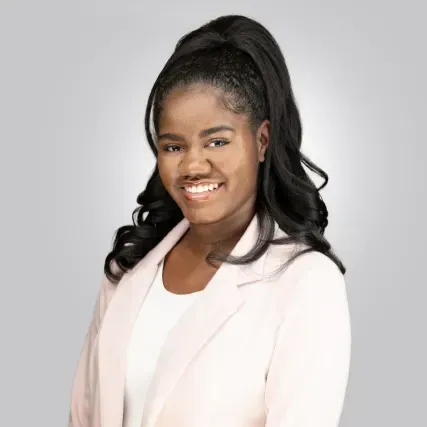 Portrait of a smiling person in a light pink blazer against a gray background