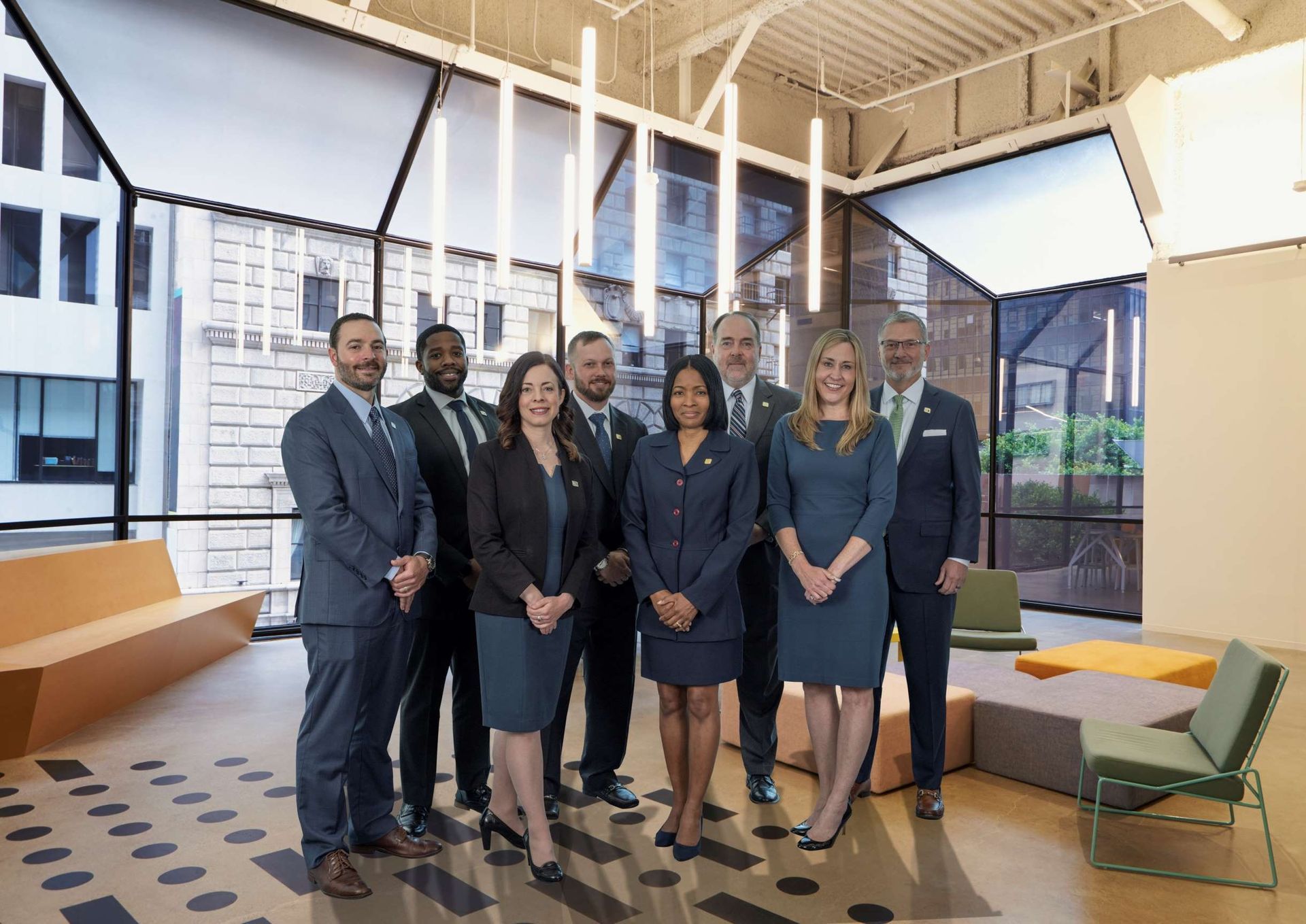 Six professionals standing in a bright modern office with large windows and city views