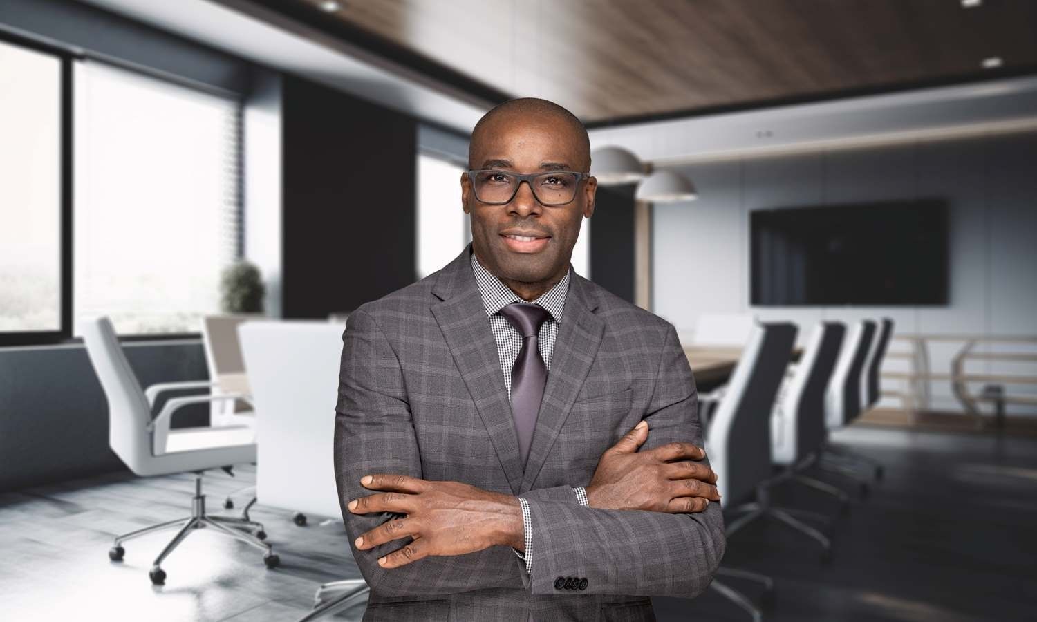 Professional man in a gray suit stands with arms crossed in a modern office conference room.