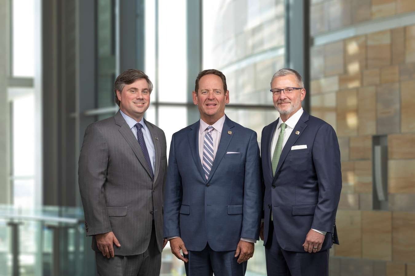 Three men in suits standing in a modern office lobby