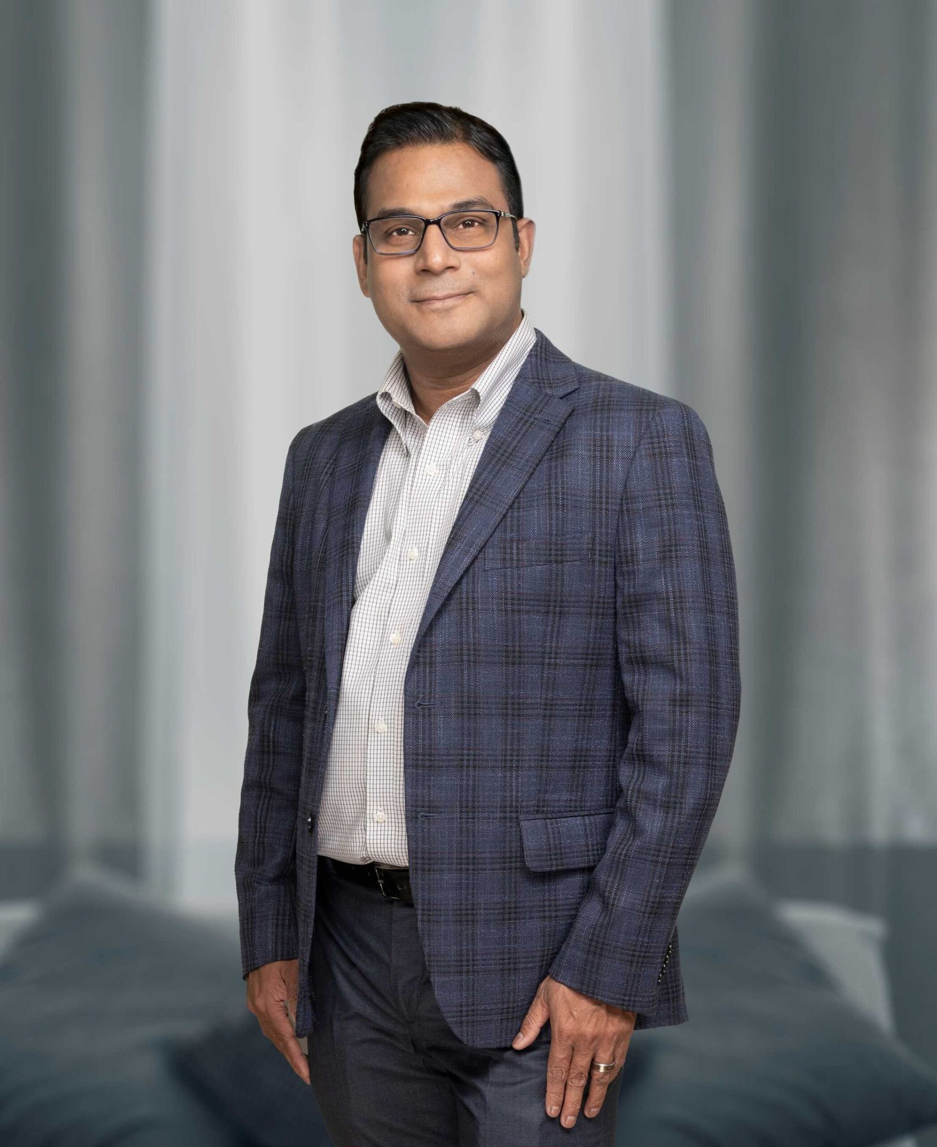 Man in a blue plaid suit standing indoors against a gray curtain backdrop