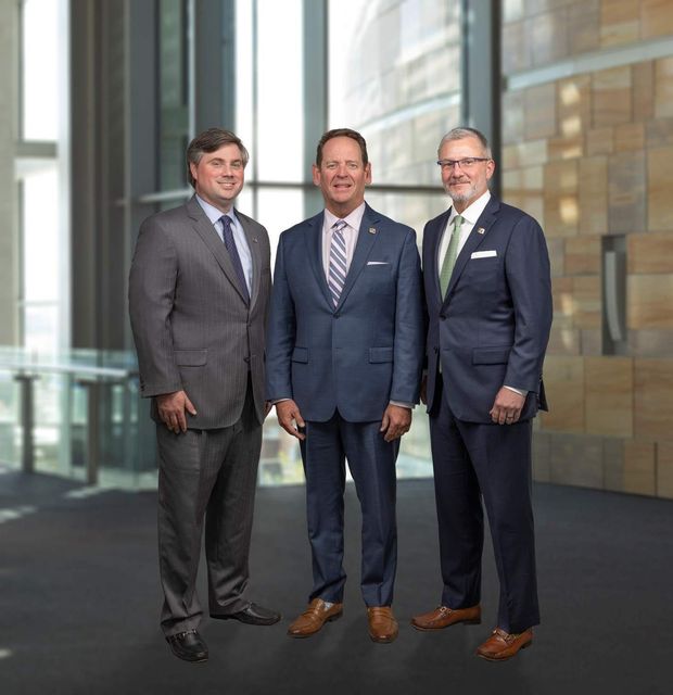 Three men in suits standing together in a modern building lobby.