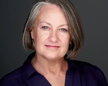 Studio portrait of a woman with gray hair in a dark blouse, facing forward with a slight smile