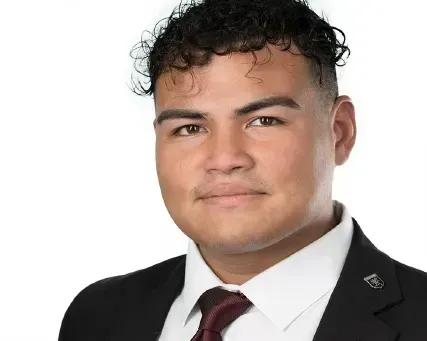 Studio portrait of a person in a black suit, white shirt, and burgundy tie, against a white background