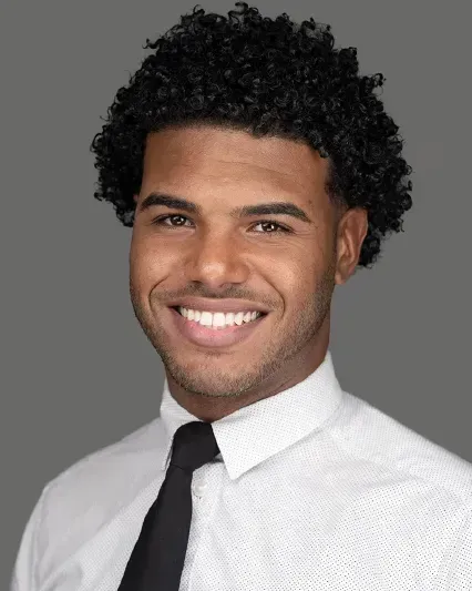 Smiling man in a white dress shirt and black tie against a gray background