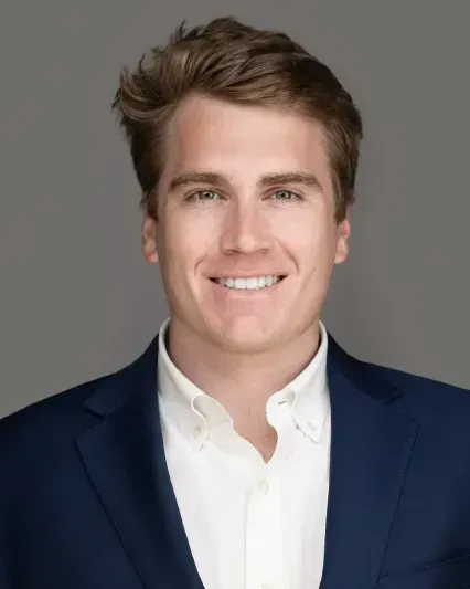 Smiling person in a navy blazer and white shirt against a gray background