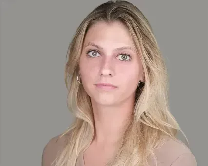 Portrait of a blonde woman against a gray background, looking directly at the camera.