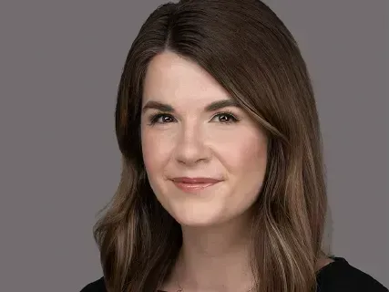 Portrait of a woman with long brown hair against a gray background, slight smile
