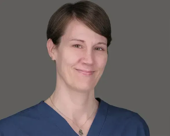 Smiling person in blue scrubs against a gray background