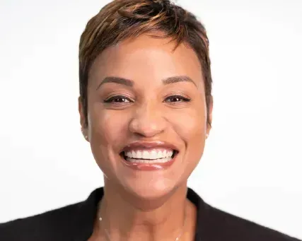 Smiling person with short hair against a white background, wearing a black top.