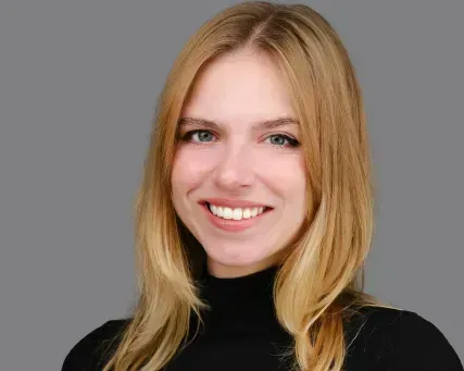 Smiling blonde person in a black turtleneck against a gray background