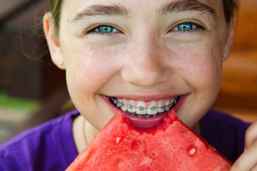 A young girl with braces is eating a slice of watermelon.