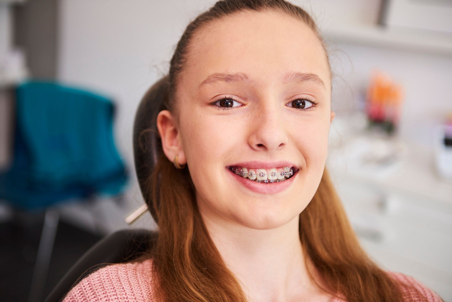 A young girl with braces is smiling while sitting in a dental chair.