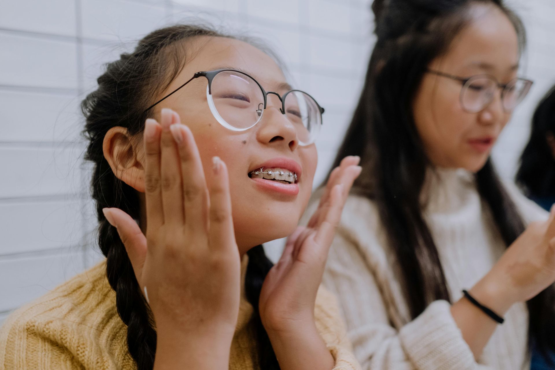 A girl with braces on her teeth is clapping her hands.