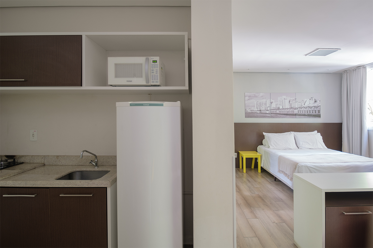Uma cozinha com geladeira, micro-ondas, pia e cama.