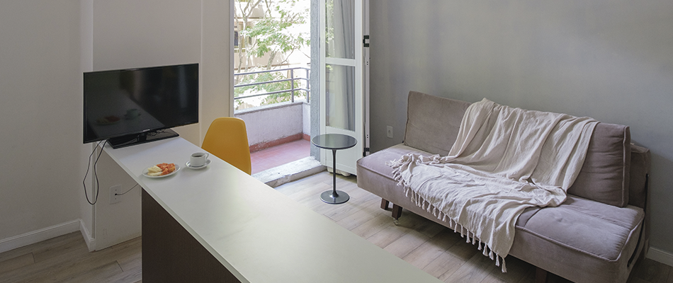 Uma sala com sofá, mesa, televisão e varanda.