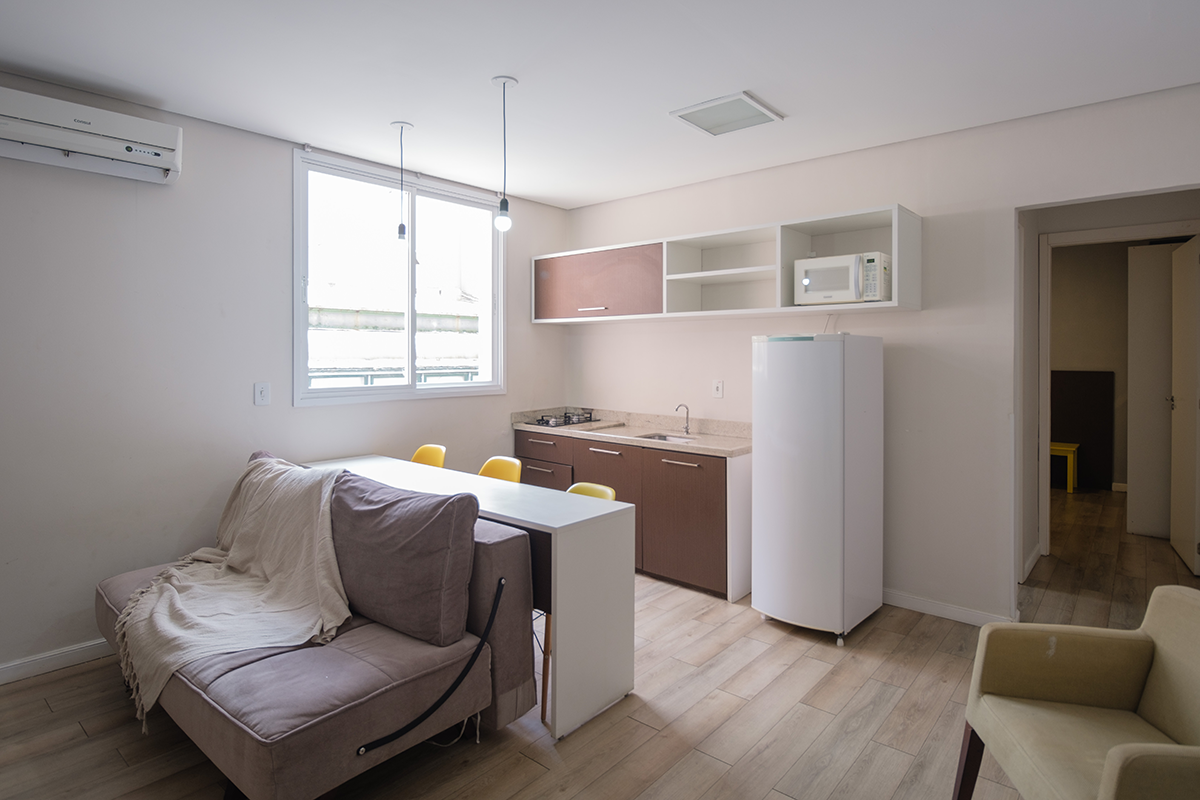 Uma sala com sofá, cadeira, mesa e geladeira.