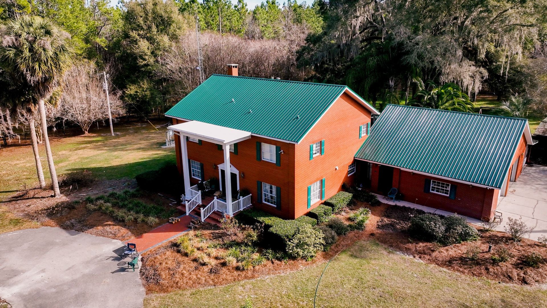 Small orange cabin with green roof and porch, beside a matching outbuilding in a wooded yard.