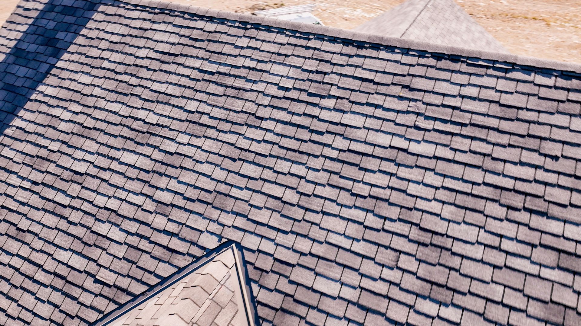 An aerial high-angle view showing a newly installed, neatly layered dark gray asphalt shingle roof