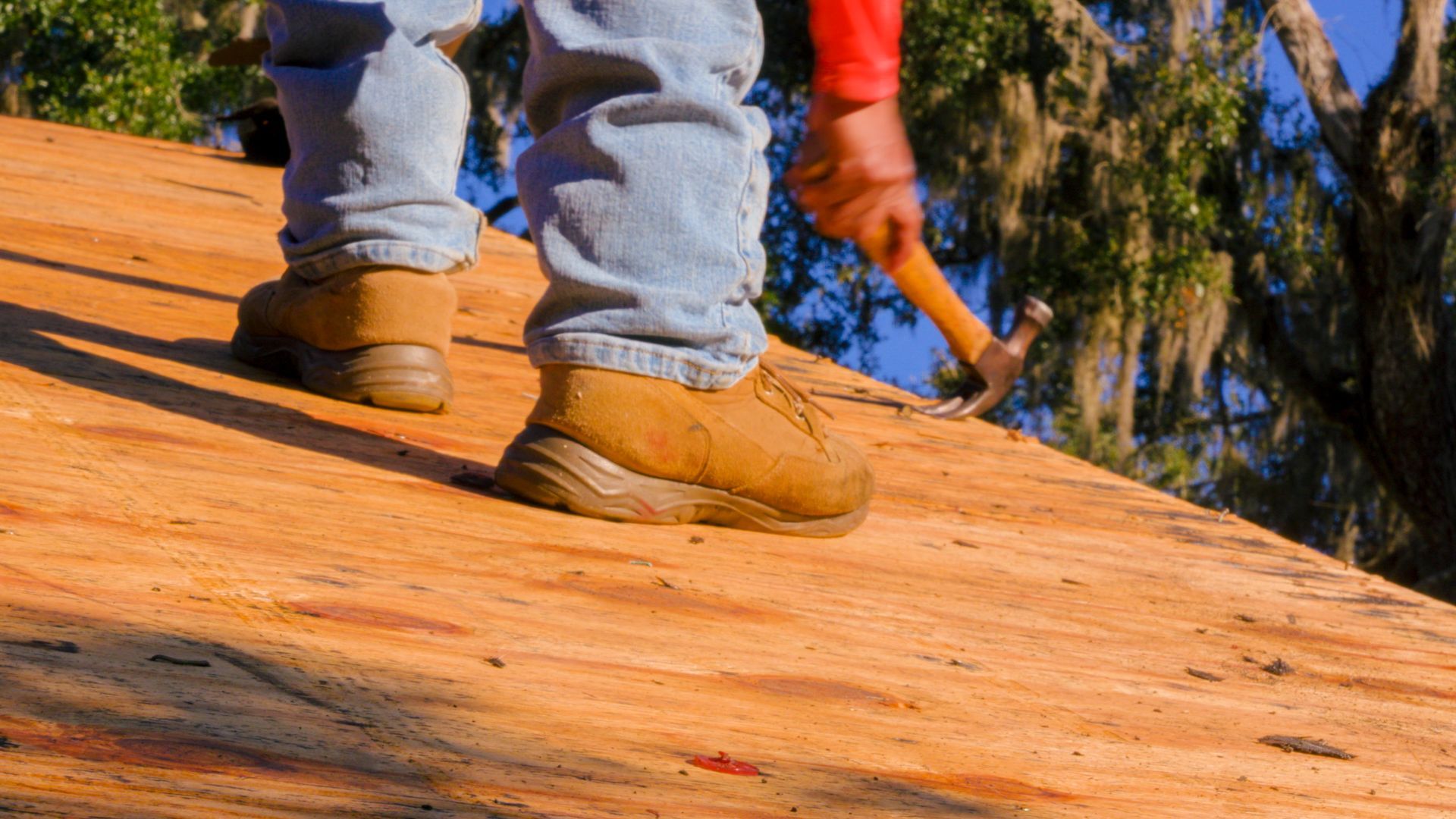Roofer using a hammer on a plywood roof deck during a Keeler Roofing installation project.