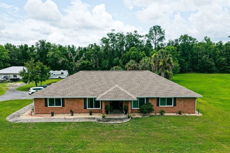 Single-story brick home with a pitched roof surrounded by green lawn and trees 