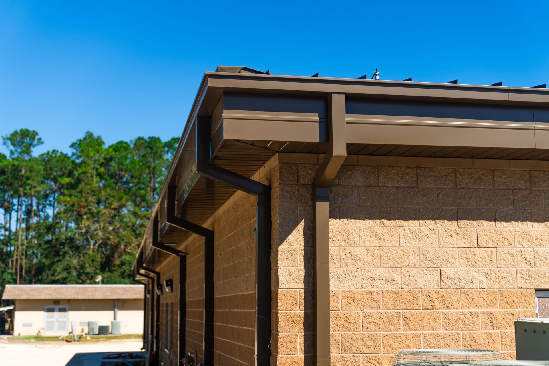 Brown brick building exterior with a roof overhang and white trim under a clear blue sky