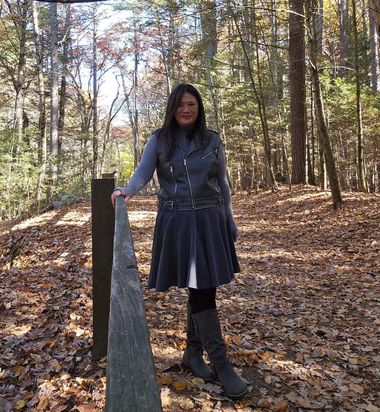 A woman in a skirt and boots is standing in the woods