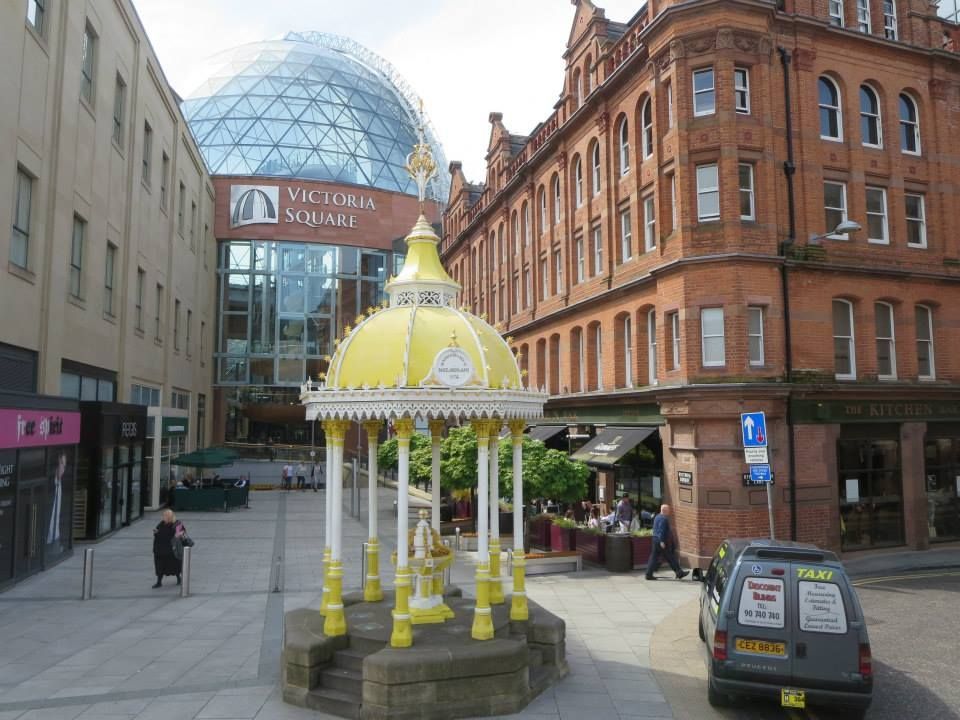A yellow gazebo in front of a building that says victoria square