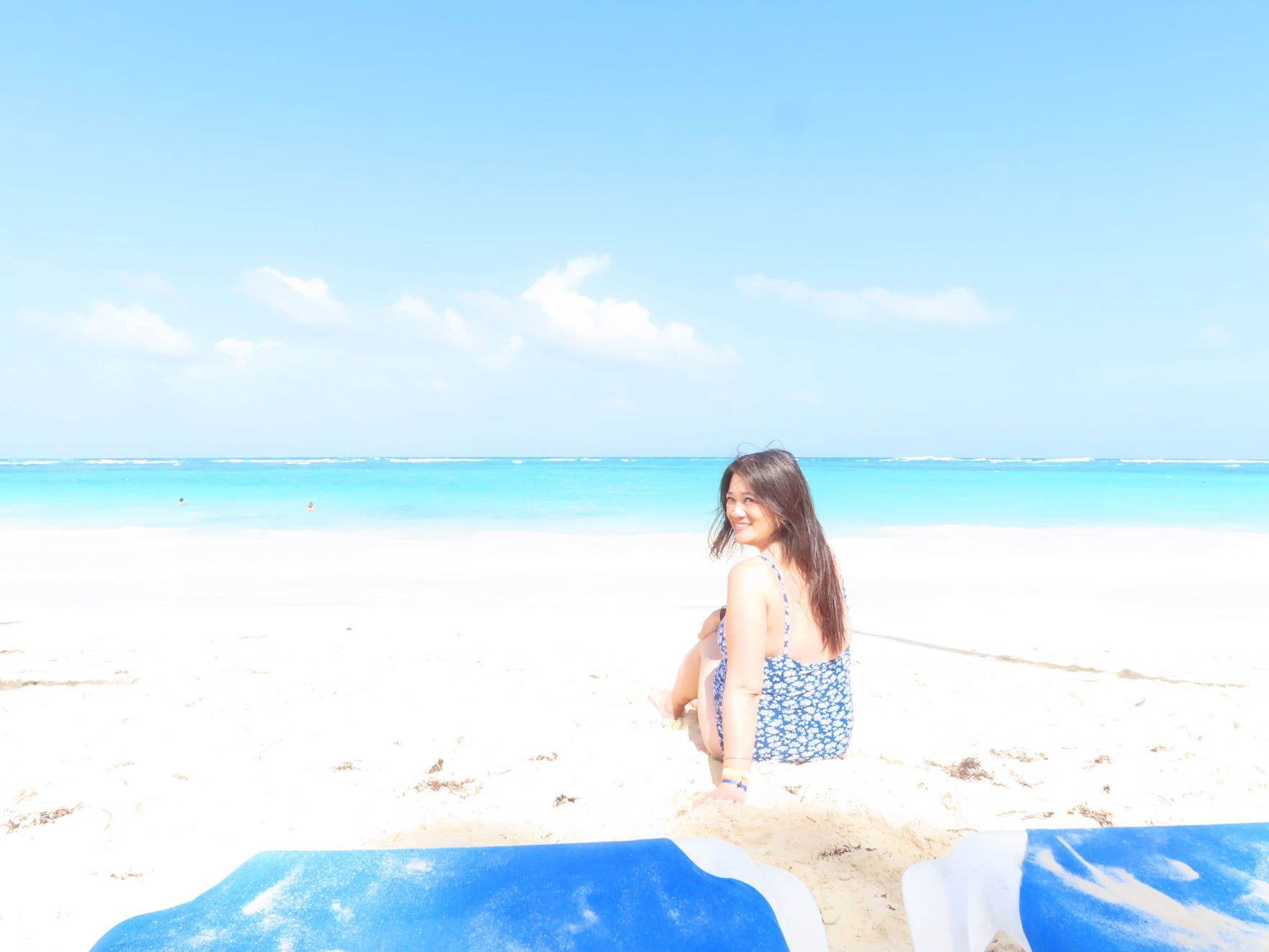 A woman is sitting on the beach looking at the ocean.